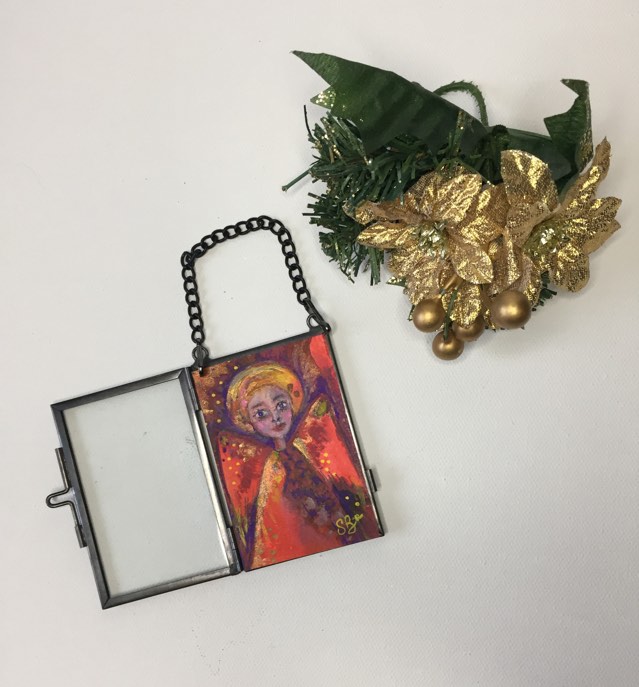 Special Christmas Angel - hanging decoration. The angel is painted with red, gold and purple tones. She is encased in a glass frame that can hang on your Christmas tree or on the wall.