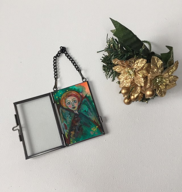 Special Christmas Angel - hanging decoration. The angel is painted with green and gold tones. She is encased in a glass frame that can hang on your Christmas tree or on the wall.