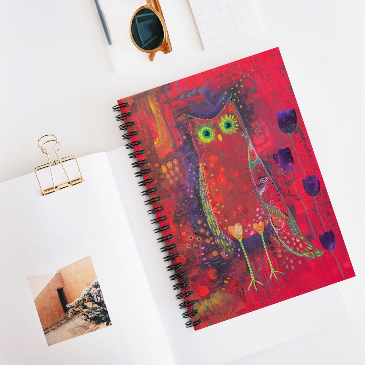 Owl journal in context- Ruby Owl is a whimsical owl painted in hues of red and purple with yellow and green pattern detail. Purple tulips grow beside her.