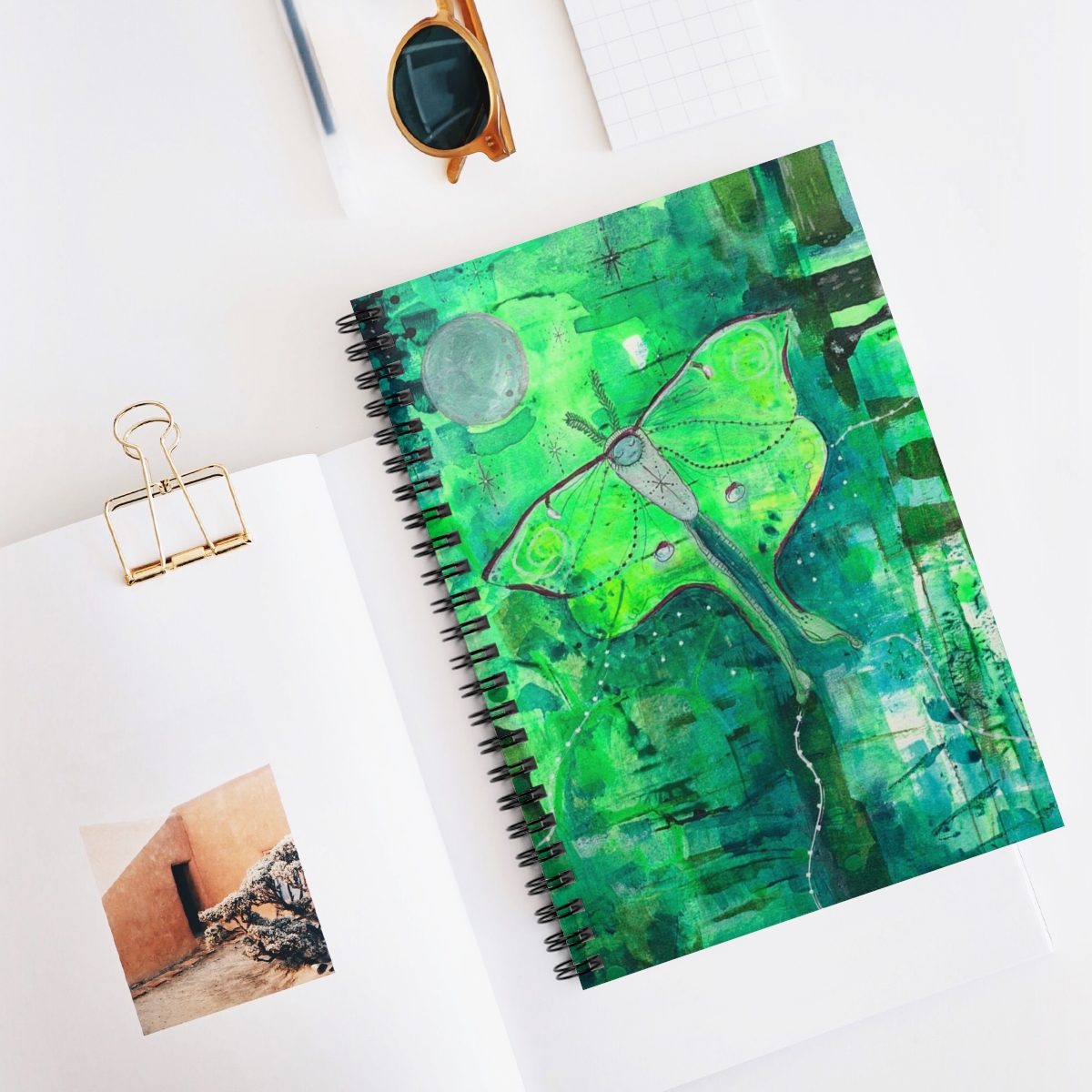 Special luna moth journal in context. Luna moth is a whimsical painting. The moth flies against a background of striking greens towards the moon.