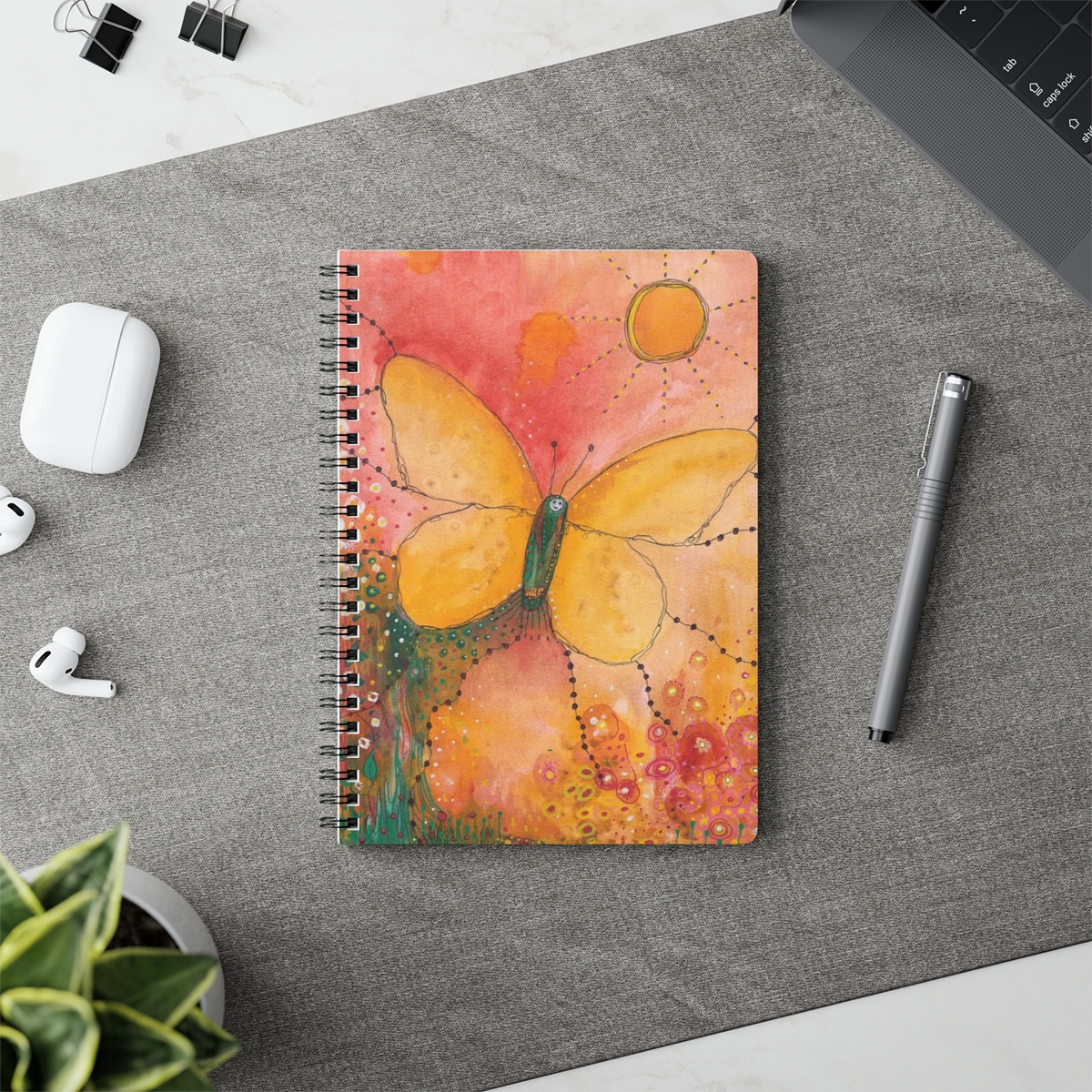 Butter fly notebook in context. Image of butterfly uses soft tones of yellows and oranges and the butterfly is rising to greet the sun