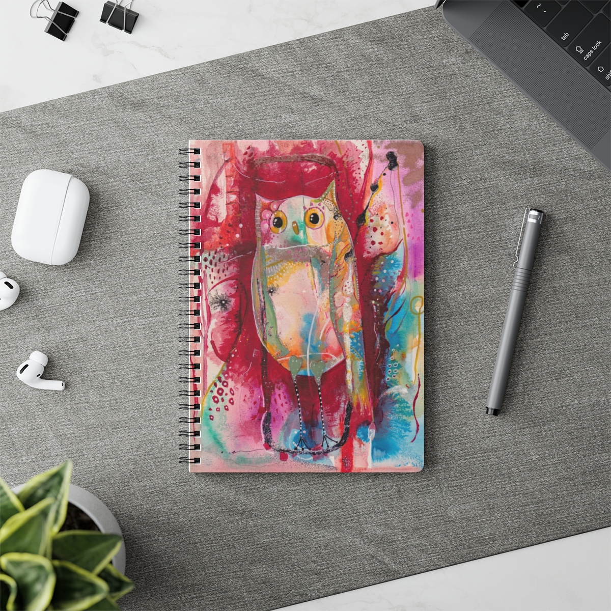 Whimsical owl notebook in context- Owl is multi-coloured on an abstract background.