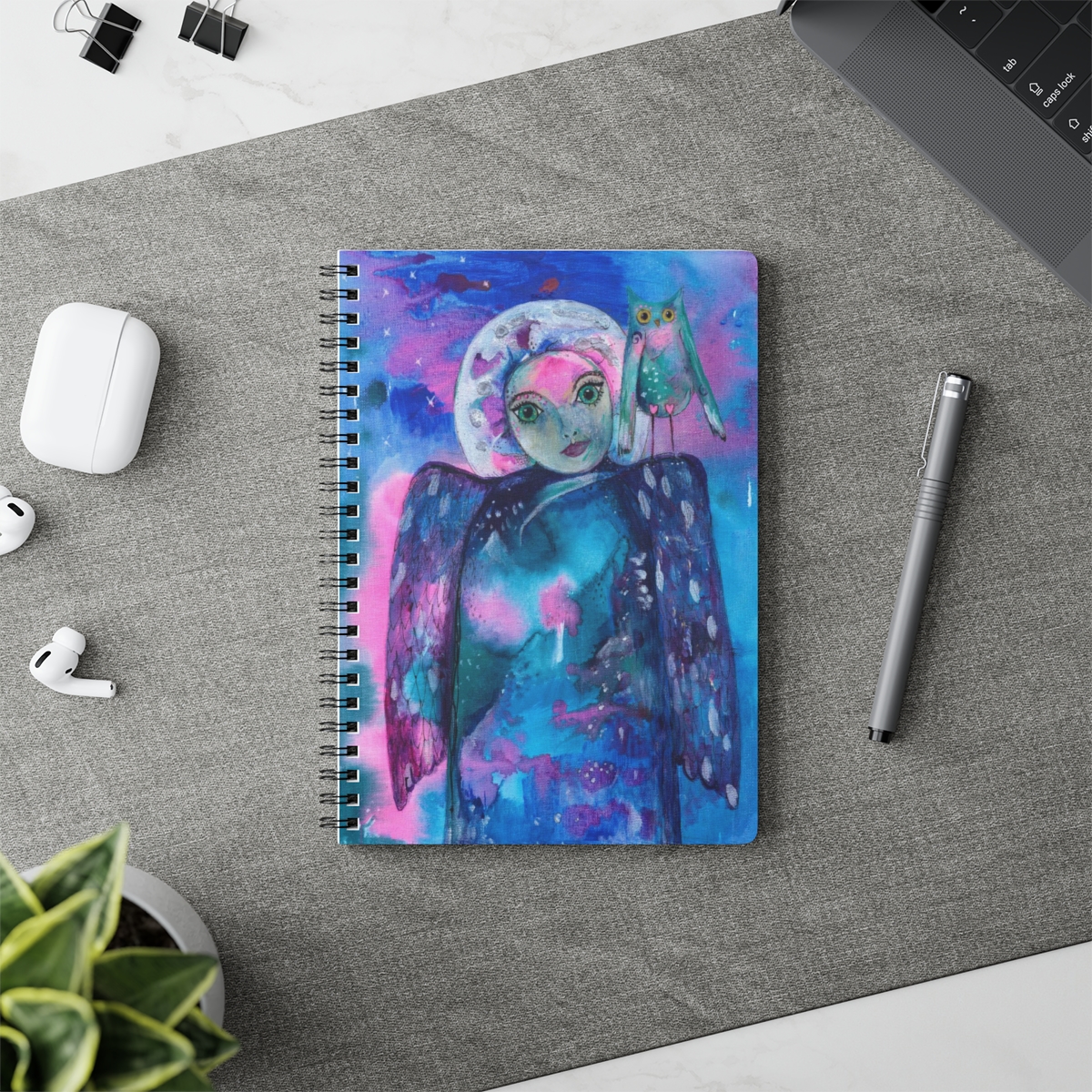Angel notebook in context. It takes the image - guardian angel of Intuition - she is created from abstract blues and pinks. Her moon like face is surrounded by a silver halo and she has an owl on her shoulder.