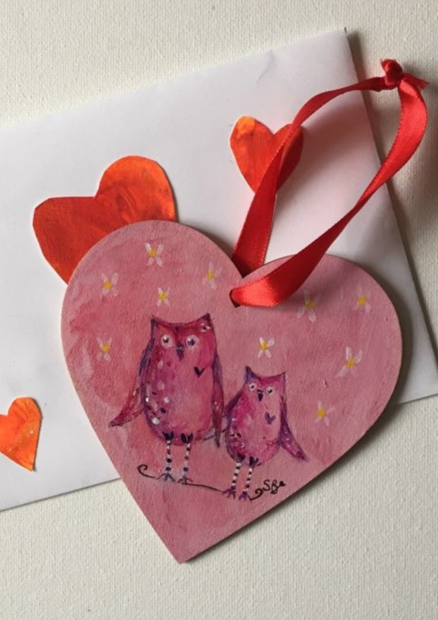 Cute owl art on hanging heart - pink background with two owls holding wings painted in pinks and purples.