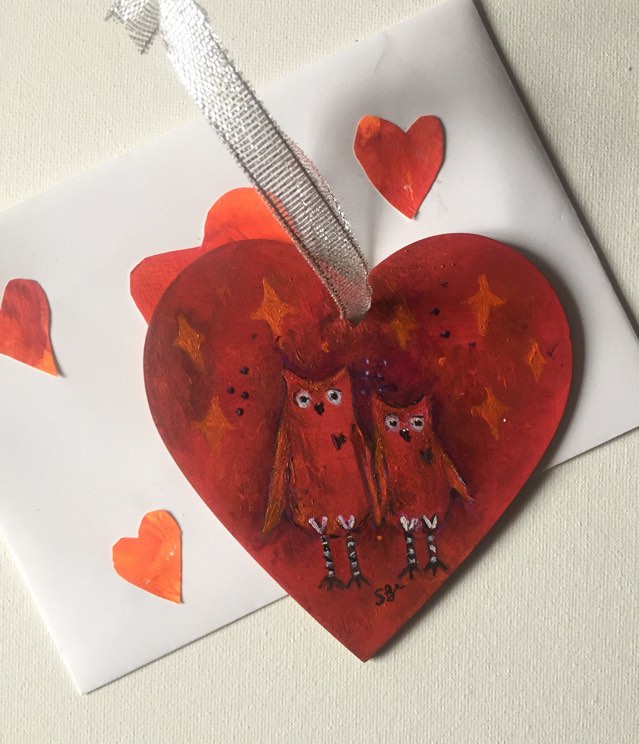 Cute owl art on hanging heart -red and purple background with two red owls holding wings and orange jewel/star motifs.