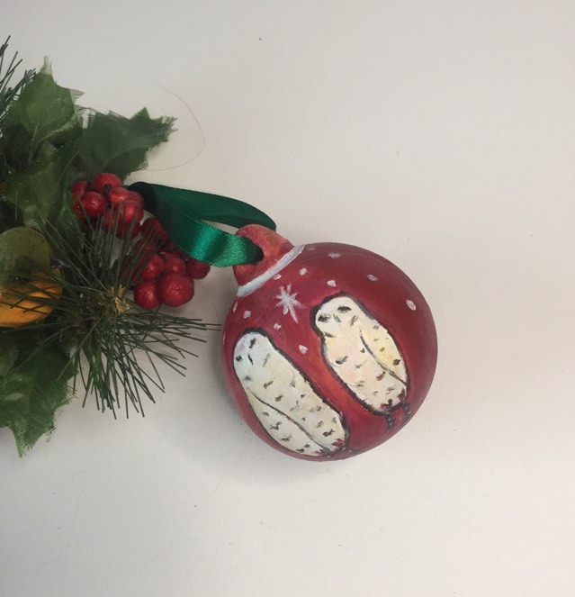 Red keepsake Christmas bauble with green ribbon. Hand painted with two snowy owls standing under a white star with snow falling