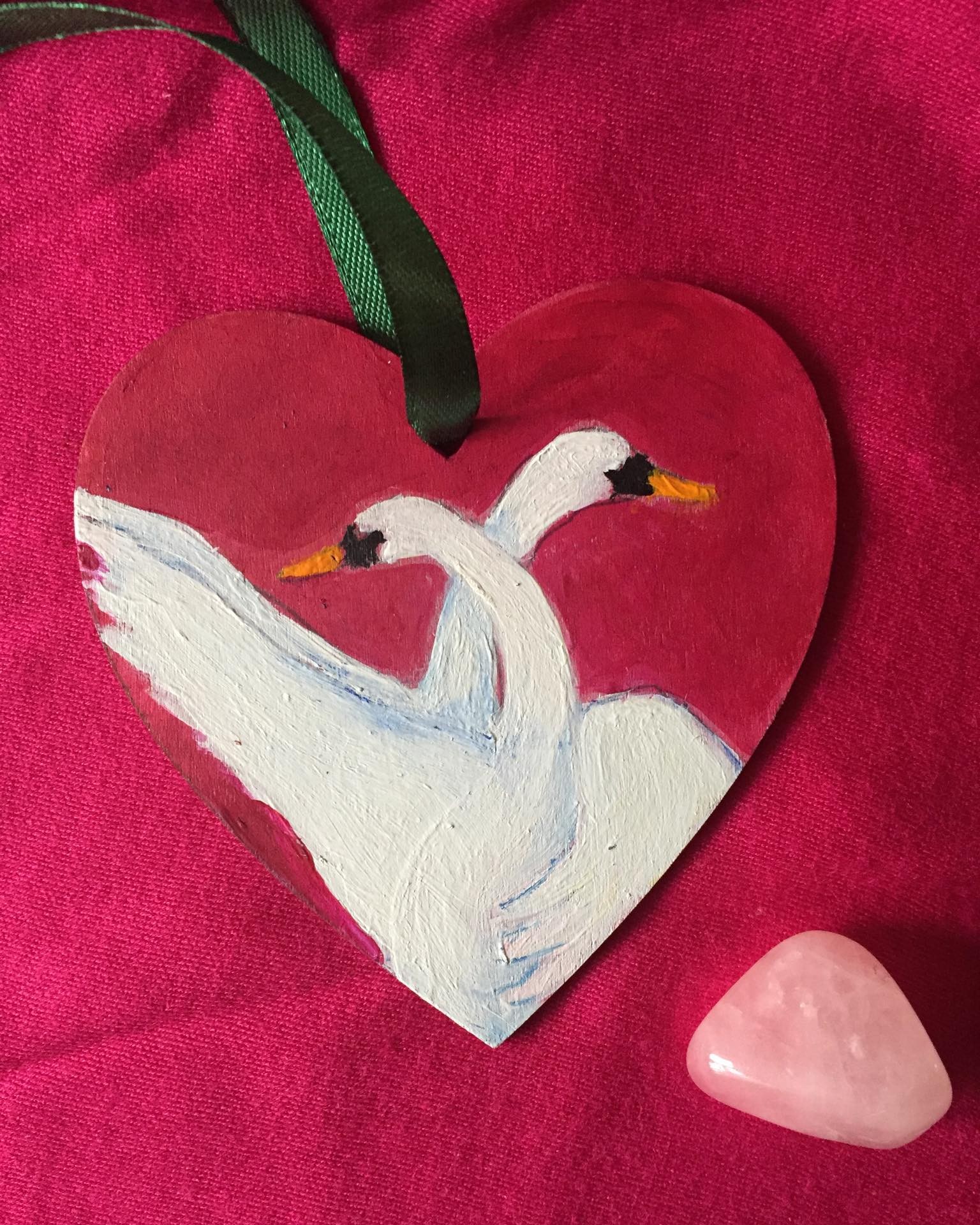 hand painted wooden heart with 2 swans dancing a waltz on a background of magenta.