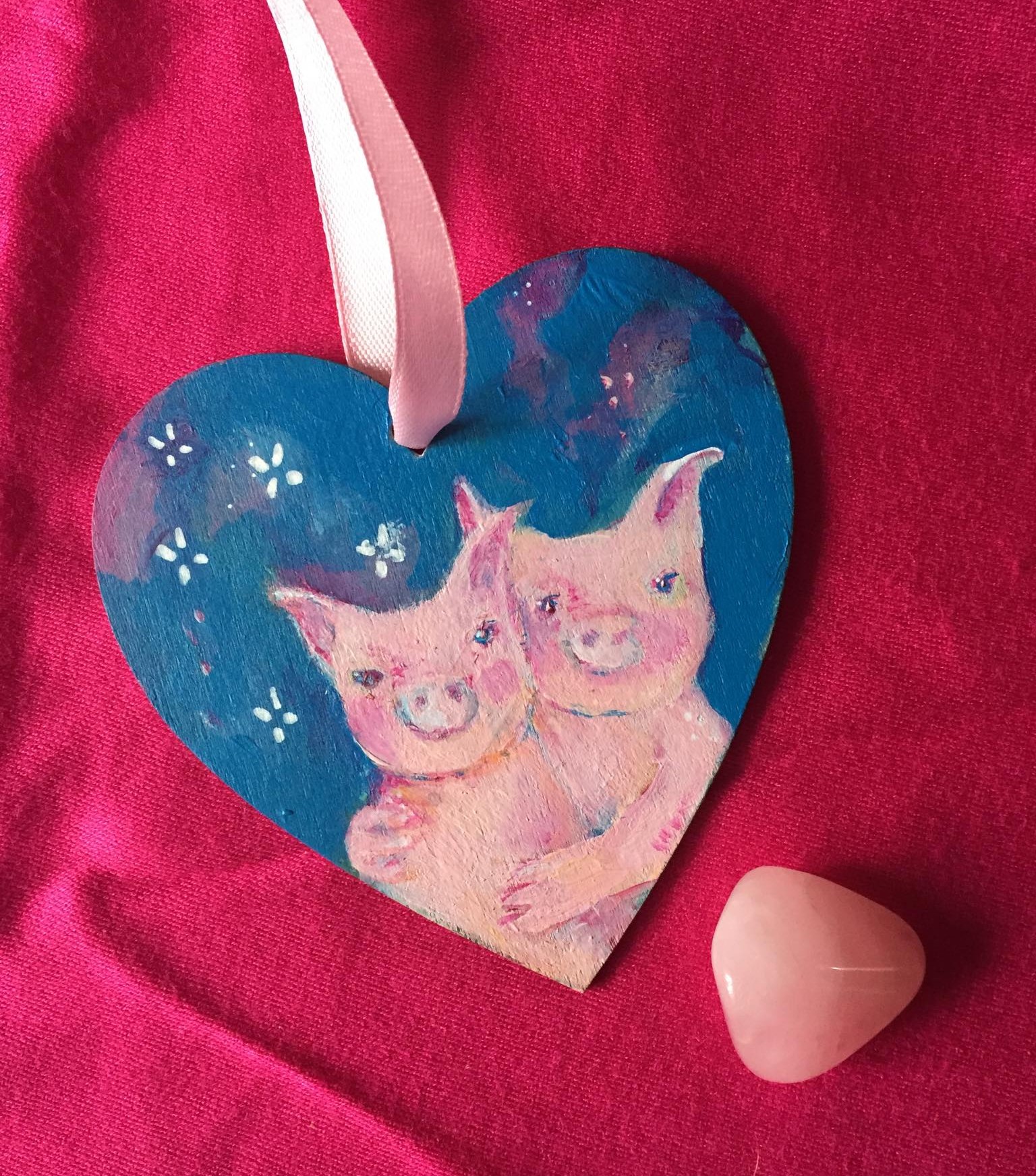 hand painted wooden heart with 2 pigs hugging against a blue background dotted with daisies.
