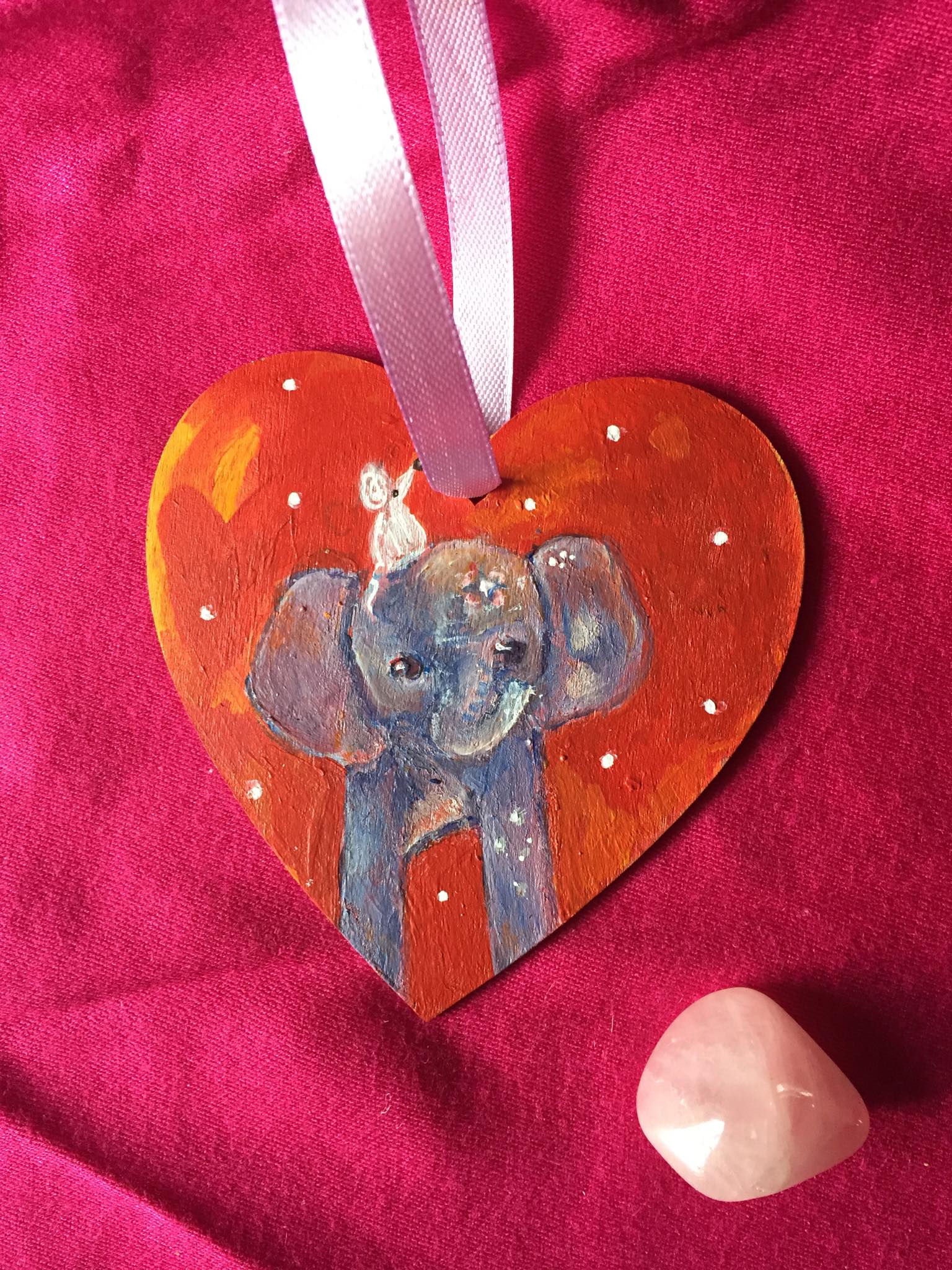 hand painted wooden heart with an elephant carrying a mouse on her head on a red background.