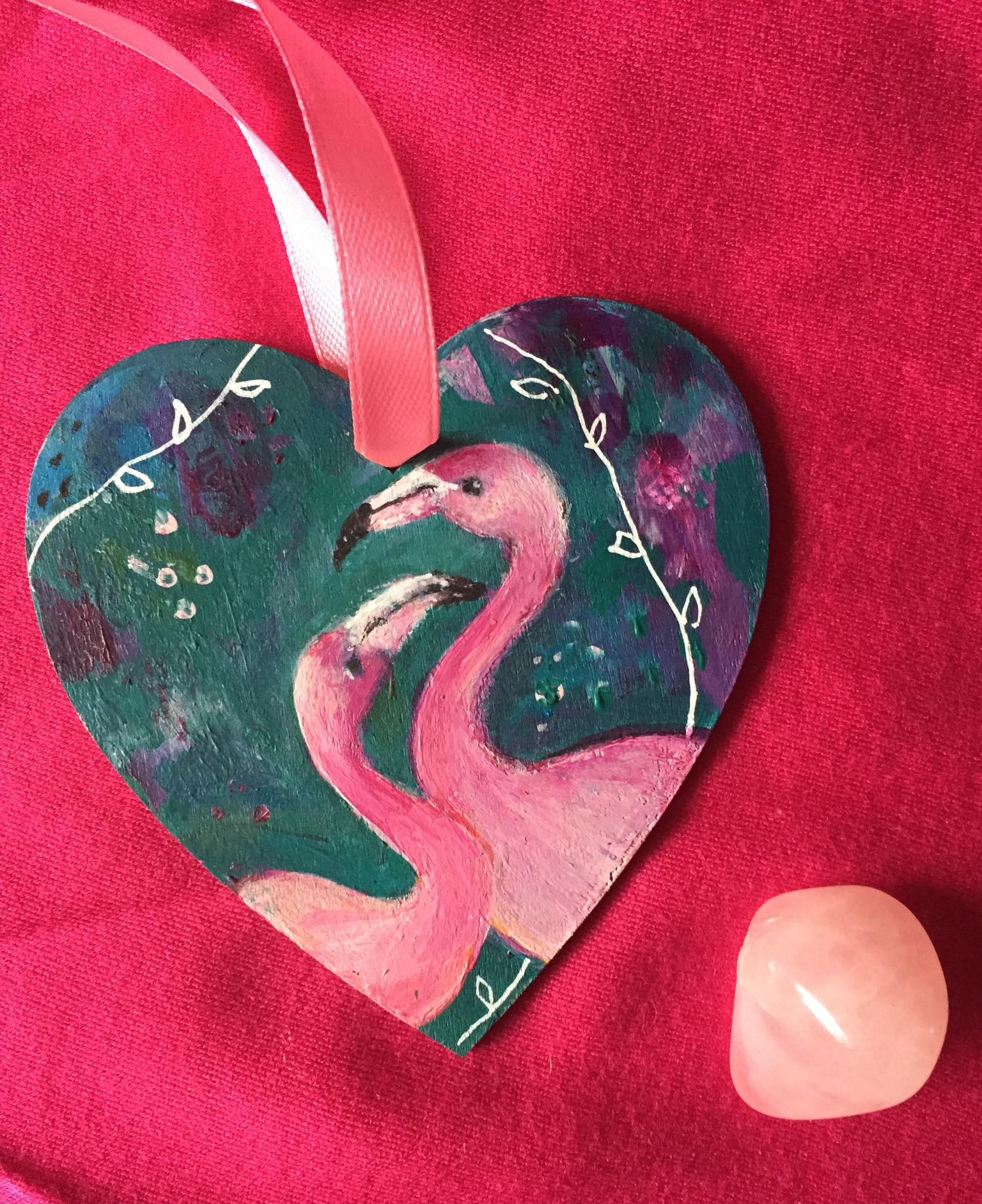 hand painted wooden heart with 2 flamingos and whimsical plants on a green and pink background.